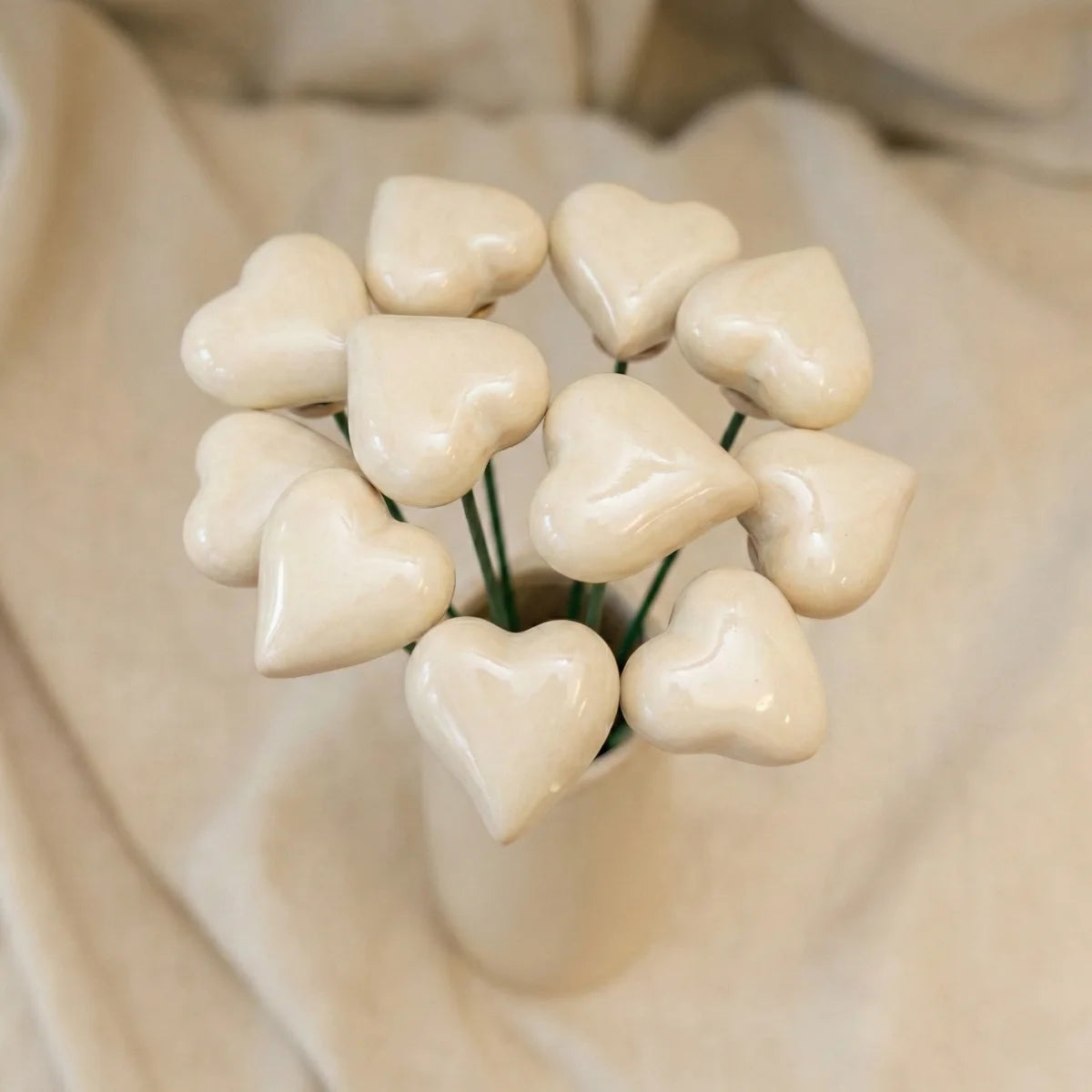 Ein kleines rotes Herz aus Keramik an einem silbernen Drahtstiel in einem Blumentopf.