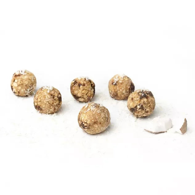 Weiße Schale mit Kraft-Kugeln mit Kokos und Vitamin B-Komplex auf hellem Hintergrund, bereit zum Verzehr.