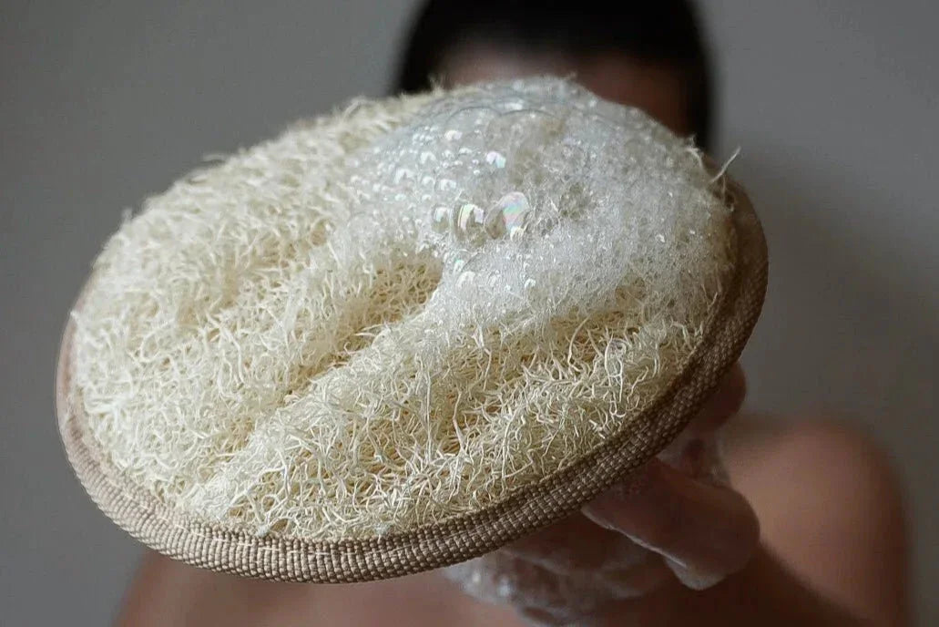 Ein rundes, beiges Loofah Körperpad mit einer Schlaufe auf einer hellen Oberfläche