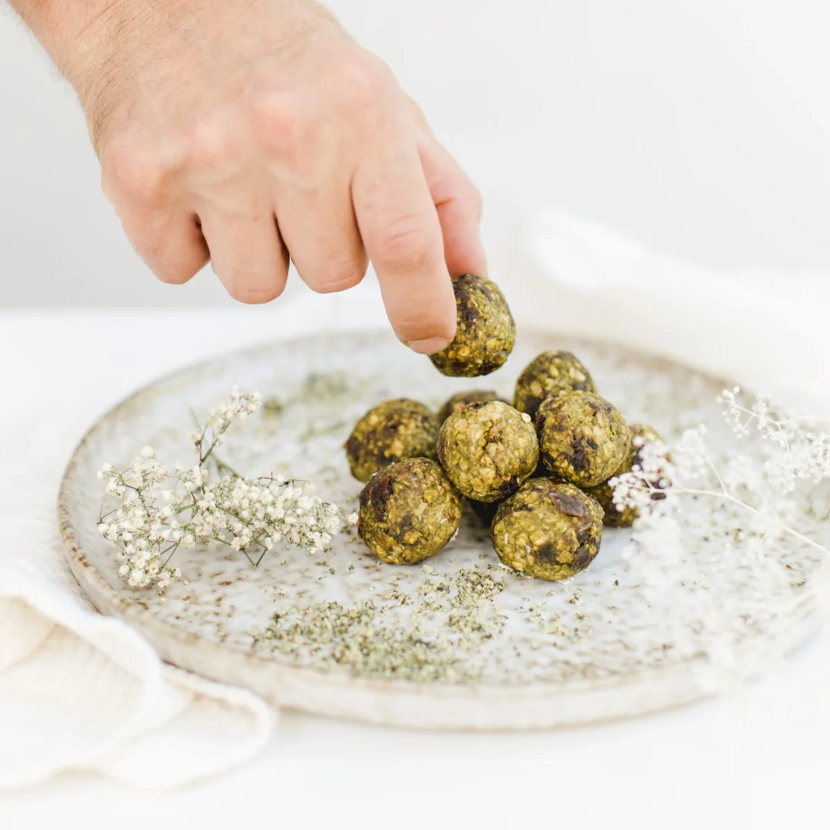 Drei grüne Matcha Power-Kugeln liegen dekorativ neben einer kleinen Schale mit Teepulver.