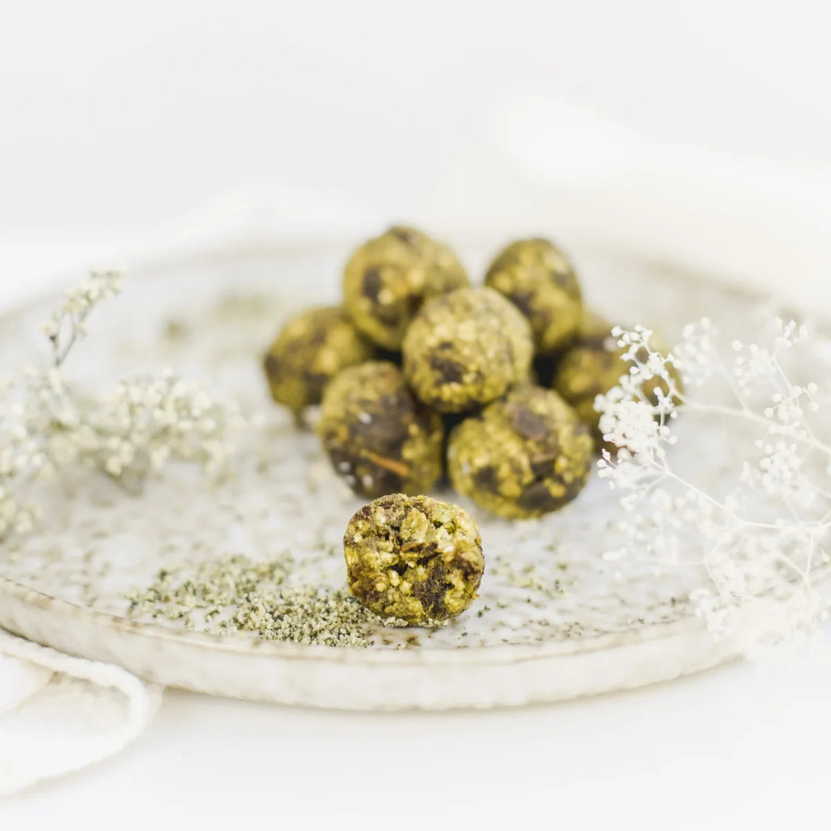 Drei grüne Matcha Power-Kugeln liegen dekorativ neben einer kleinen Schale mit Teepulver.