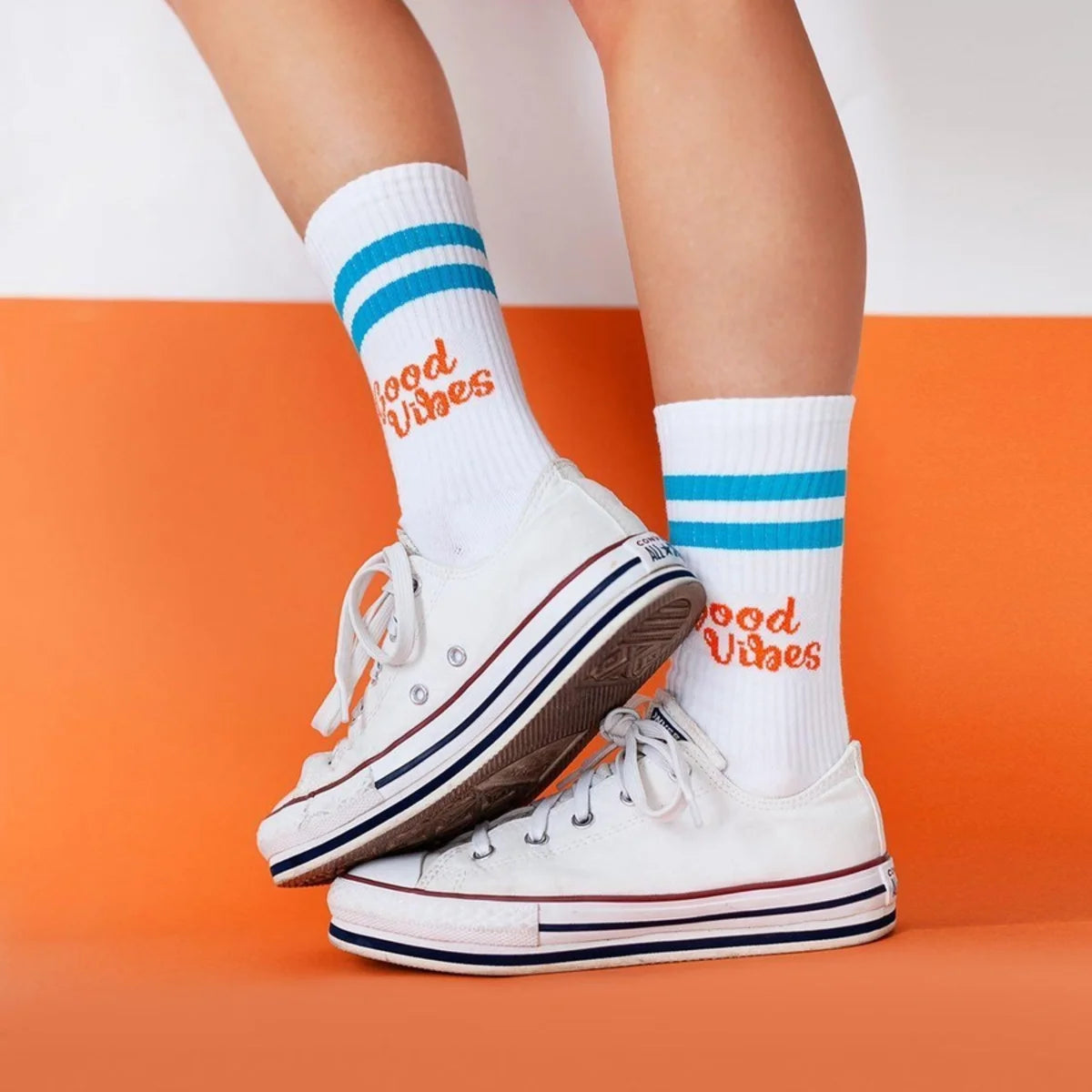 Blaue und orange Sportsocken aus Baumwolle mit aufgedrucktem Spruch „Good Vibes" auf weißem Hintergrund.