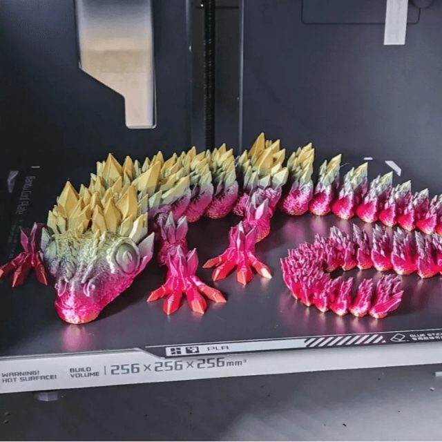 Beweglicher 3D-gedruckter Drache mit Farbverlauf von Gelb zu Pink auf der Druckplatte