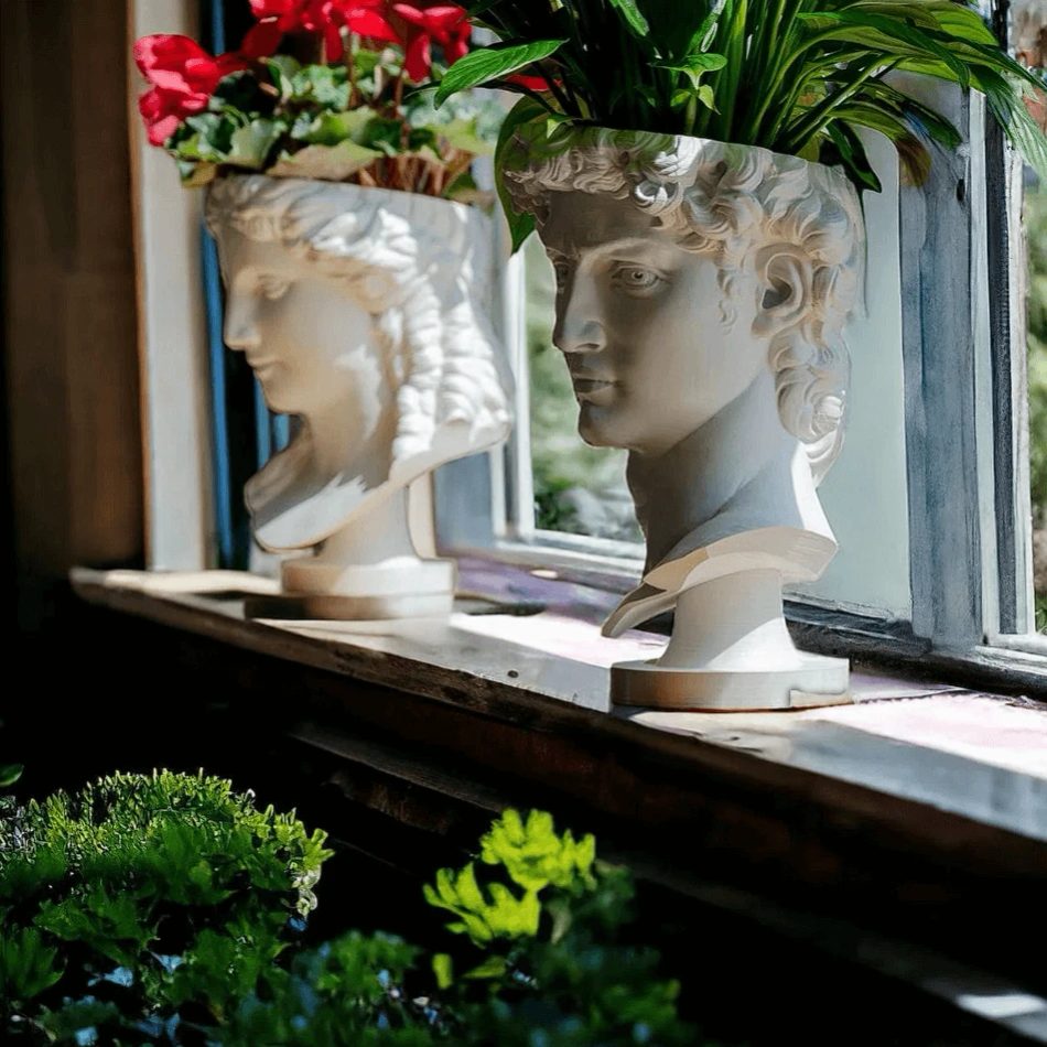Zwei 3D-gedruckte Pflanzentöpfe in Form antiker Büsten aus Marmor-Filament, bepflanzt, auf einer Fensterbank