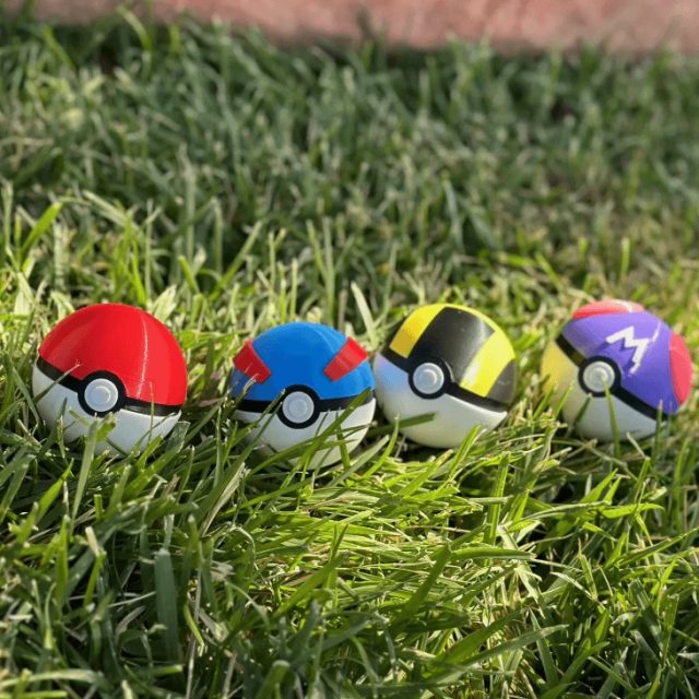 Vier 3D-gedruckte Pokébälle in verschiedenen Farben im Gras