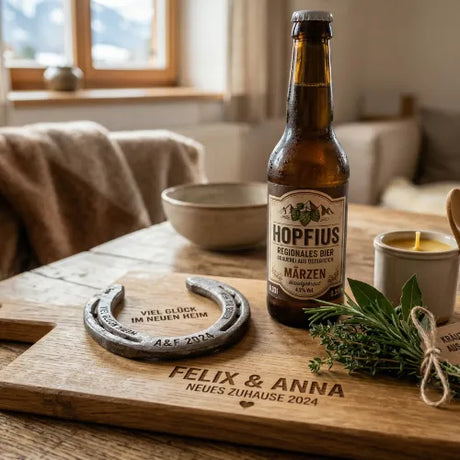 Graviertes Holzbrett mit Hufeisen „Viel Glück im neuen Heim“, Bierflasche Hopifus, frischen Kräutern und Kerze in gemütlicher Wohnumgebung.