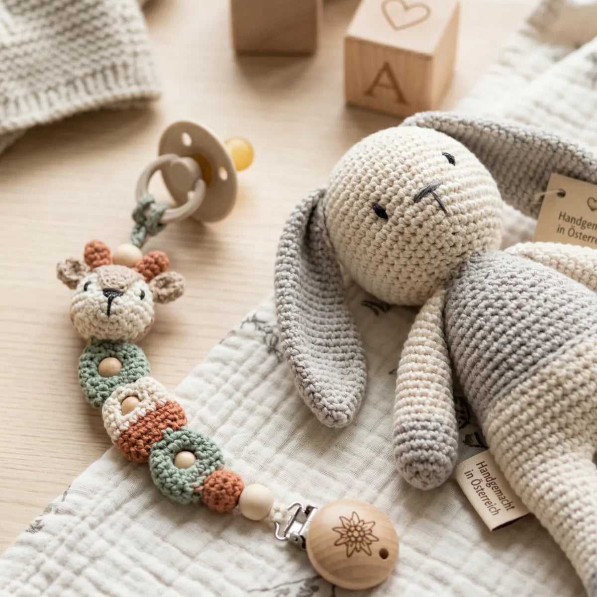 Bunte, handgemachte Holzbausteine und ein weiches Stofftier, umgeben von Babykleidung, als Geschenkidee für Kinder