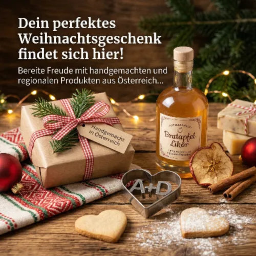 Ein verpacktes Weihnachtsgeschenk mit 'Handgemacht in Österreich'-Anhänger, umgeben von einem Bratapfellikör, Zimtstangen, getrockneten Apfelscheiben und Herz-Keksen auf rustikalem Holz
