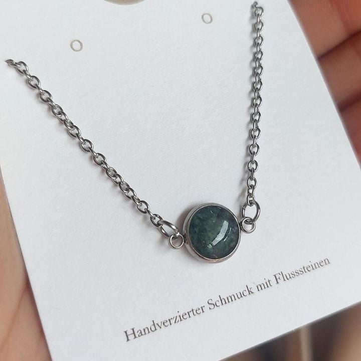 Halskette aus Edelstahl mit einem handgesammelten Flussstein-Anhänger, gefertigt von Steinschmuck Austria. Das Design vereint modernen Edelstahlschmuck mit einem natürlichen Stein, der in der Mitte des Anhängers eingefasst ist. Perfektes Accessoire für Naturverbundene, handgemacht in Österreich.