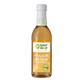 Eine Glasflasche mit hellem Akazienblüten Sirup der Marke Green Sheep, umringt von zarten Akazienblüten und Blättern.