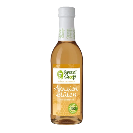 Eine Glasflasche mit hellem Akazienblüten Sirup der Marke Green Sheep, umringt von zarten Akazienblüten und Blättern.