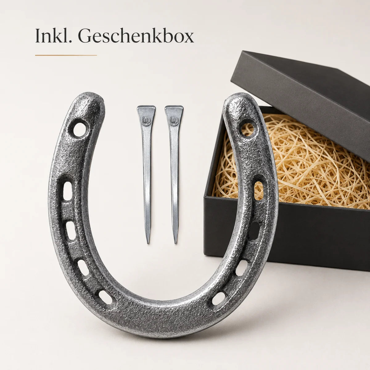 Geschenkset mit einem silbernen Gusseisen-Hufeisen und zwei Hufnägeln in einer schwarzen mit Stroh ausgelegten Geschenkbox.