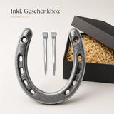 Geschenkset mit einem silbernen Gusseisen-Hufeisen und zwei Hufnägeln in einer schwarzen mit Stroh ausgelegten Geschenkbox.