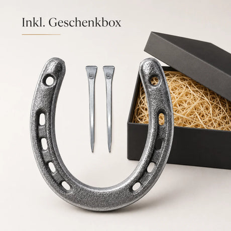 Geschenkset mit einem silbernen Gusseisen-Hufeisen und zwei Hufnägeln in einer schwarzen mit Stroh ausgelegten Geschenkbox.