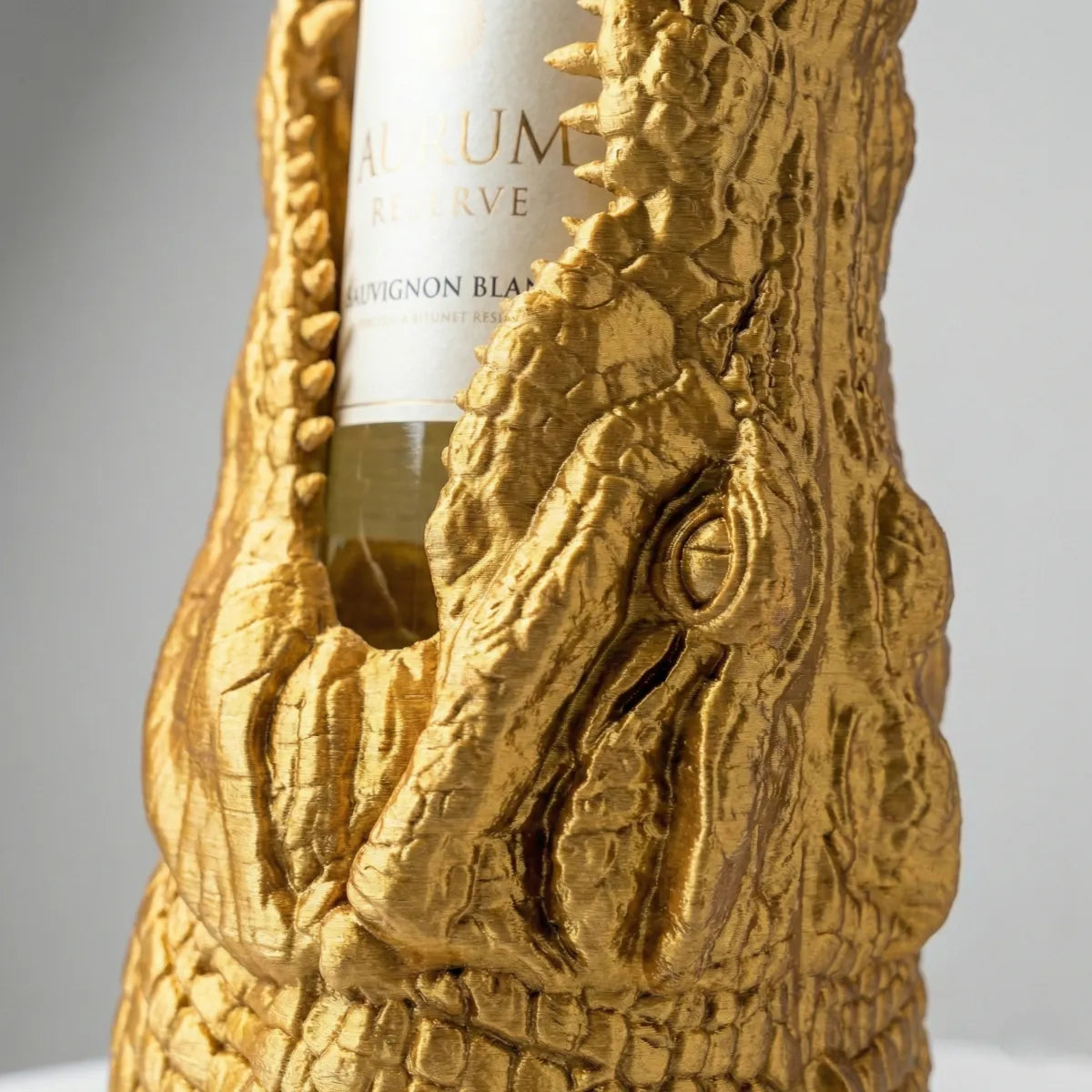 Ein dekorativer Flaschenhalter in Form eines Krokodilkopfes aus farbigem Kunststoff hält eine Weinflasche im Maul.