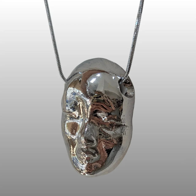 Halskette mit einem ca. 2,5 cm breiten, detailreichen Puppen-Kopf Anhänger aus weißer Keramik mit 18k Platinglasur, an einer 925er Silberkette.