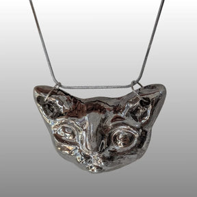 Detailaufnahme einer Halskette mit einem glasierten Sphinxkatzen-Kopf-Anhänger aus Keramik an einer feinen Silberkette.