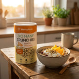 Hempions Bio Hanf Crunchies in Weiß und Orange gehalten. Detailansicht von gerösteten Hanfsamen umhüllt von weißer Kakaomasse und Orangenschalenöl in einem geöffneten Beutel.