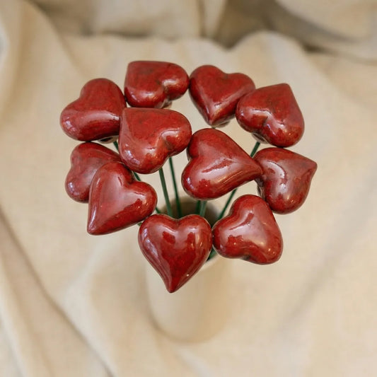 Ein kleines rotes Herz aus Keramik an einem silbernen Drahtstiel in einem Blumentopf.