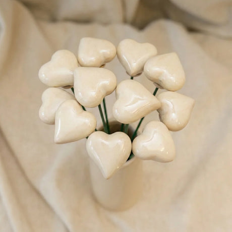 Ein kleines rotes Herz aus Keramik an einem silbernen Drahtstiel in einem Blumentopf.