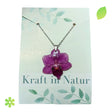 Halskette mit einer echten, lilafarbenen Orchideenblüte, eingebettet in transparentes Kunstharz, an einer silbernen Kette.