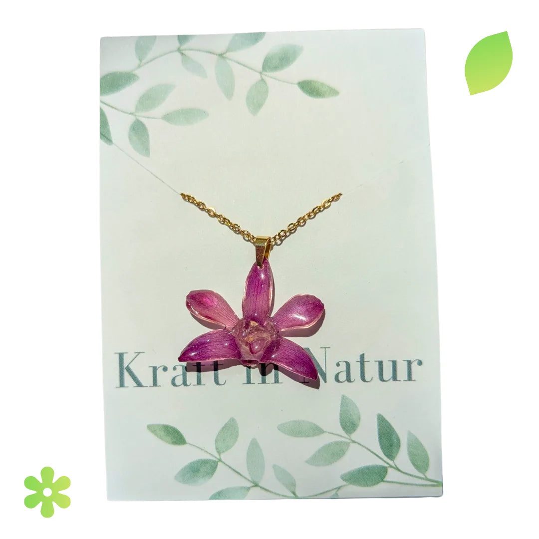Halskette mit einer echten violetten Orchideenblüte, eingebettet in transparentes Harz, an einer goldfarbenen Kette.