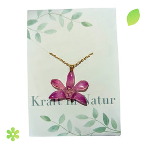 Halskette mit einer echten violetten Orchideenblüte, eingebettet in transparentes Harz, an einer goldfarbenen Kette.
