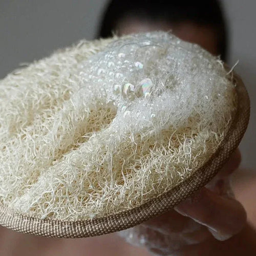 Ein rundes, beiges Loofah Körperpad mit einer Schlaufe auf einer hellen Oberfläche