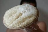 Ein rundes, beiges Loofah Körperpad mit einer Schlaufe auf einer hellen Oberfläche