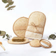 Ein Set aus vier hellen Luffa-Pflegeprodukten inklusive Handschuh und runden Pads auf einem Holzuntergrund.