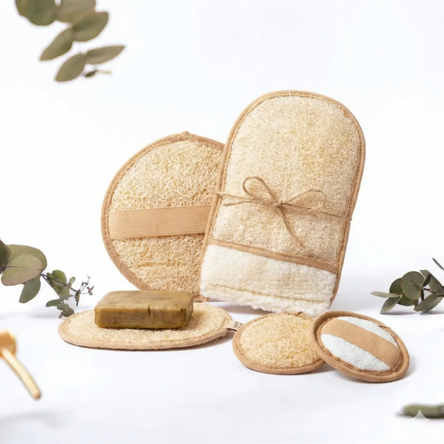 Ein Set aus vier hellen Luffa-Pflegeprodukten inklusive Handschuh und runden Pads auf einem Holzuntergrund.