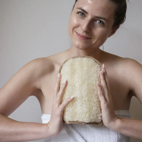 Ein rechteckiger Luffa Peelinghandschuh mit heller Baumwollseite und strukturierter Oberfläche aus Luffa-Fasern.