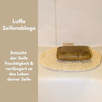 Flaches, ovales Seifenkissen aus hellbeige-farbenen Luffa-Naturfasern auf einer hellen Oberfläche