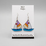 Ohrringe aus Plexiglas mit handillustriertem Segelboot-Motiv in Blau, Orange und Lila an silberfarbenen Edelstahl-Haken, Anhänger ca. 3 cm groß.