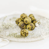 Drei grüne Matcha Power-Kugeln liegen dekorativ neben einer kleinen Schale mit Teepulver.