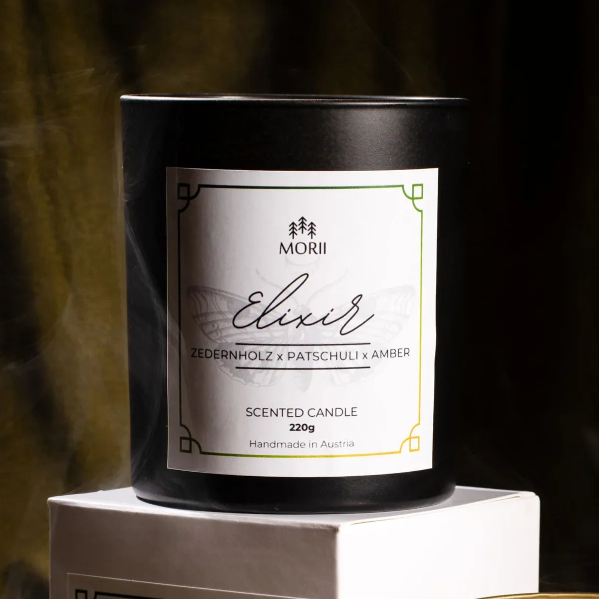 Weiße Duftkerze ELIXIR von Morii in minimalistischem Glasgefäß, umgeben von trockenen Kräutern und Blüten.