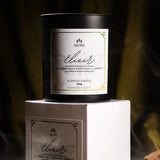 Weiße Duftkerze ELIXIR von Morii in minimalistischem Glasgefäß, umgeben von trockenen Kräutern und Blüten.