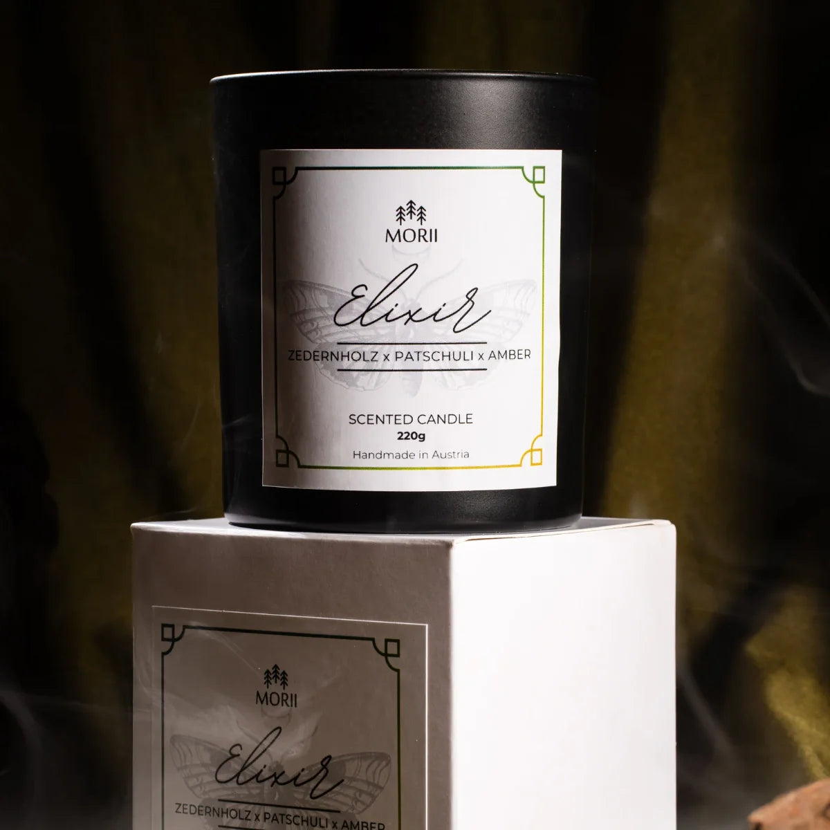 Weiße Duftkerze ELIXIR von Morii in minimalistischem Glasgefäß, umgeben von trockenen Kräutern und Blüten.