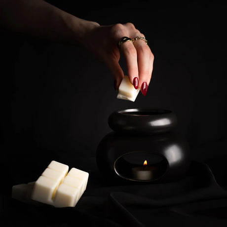 Weiße Duftkerze ELIXIR von Morii in minimalistischem Glasgefäß, umgeben von trockenen Kräutern und Blüten.