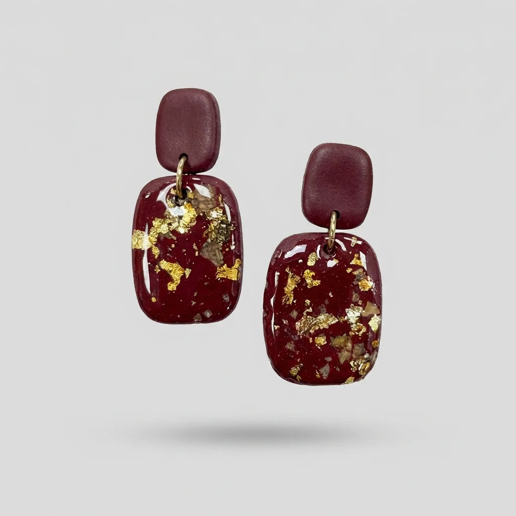 Dunkelrote Ohrringe aus Polymer Clay mit eingearbeiteten Goldflocken und Weinstein-Kristallen auf hellem Hintergrund
