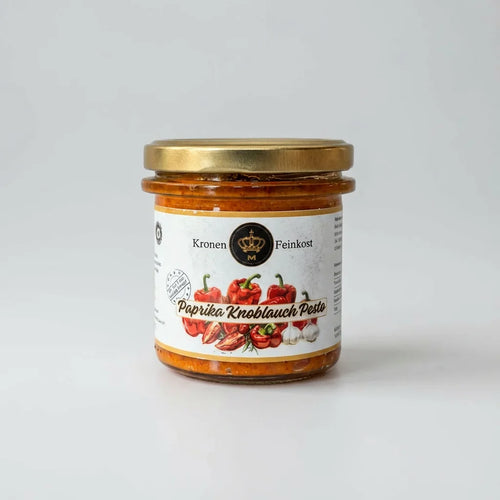 Ein Glas Paprika Knoblauch Pesto mit roter Farbe und sichtbaren Kräutern auf hellem Hintergrund.