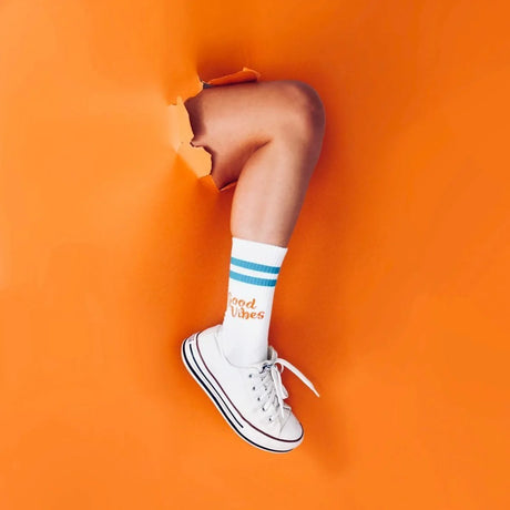 Blaue und orange Sportsocken aus Baumwolle mit aufgedrucktem Spruch „Good Vibes" auf weißem Hintergrund.
