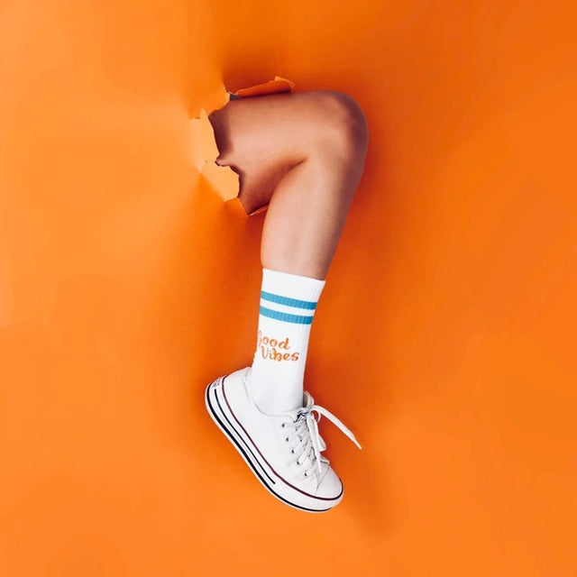 Blaue und orange Sportsocken aus Baumwolle mit aufgedrucktem Spruch „Good Vibes" auf weißem Hintergrund.
