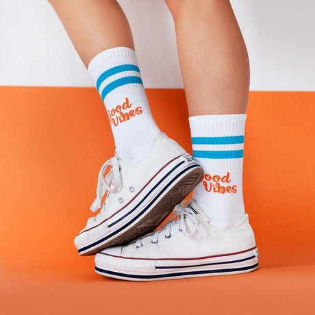 Blaue und orange Sportsocken aus Baumwolle mit aufgedrucktem Spruch „Good Vibes" auf weißem Hintergrund.