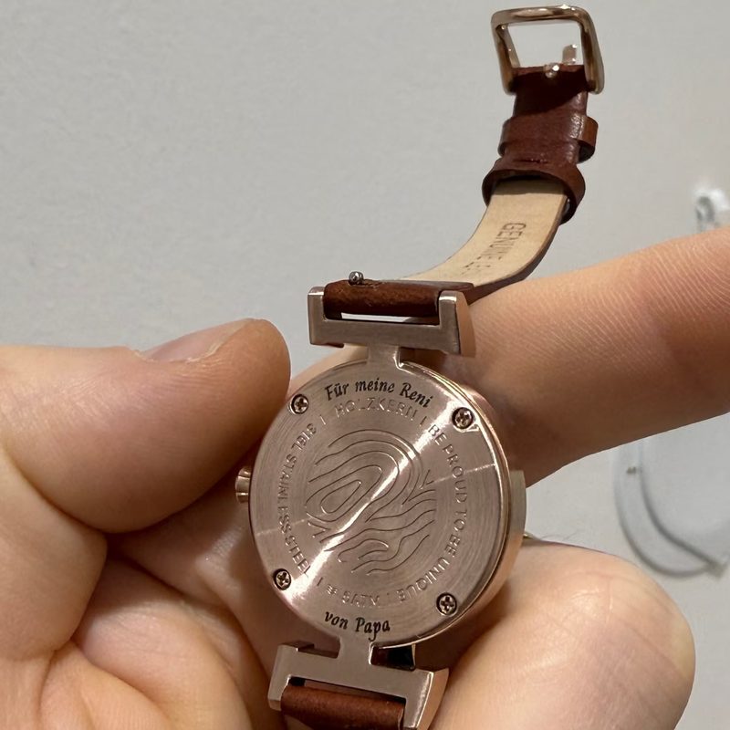 Die Rückseite einer Armbanduhr mit eingravierter Widmung wird in der Hand gehalten