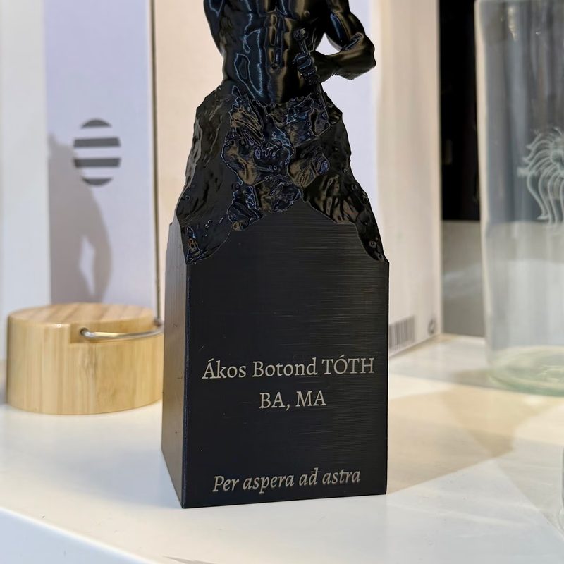 Eine dunkle Statuette auf Sockel mit graviertem Namen und akademischem Grad