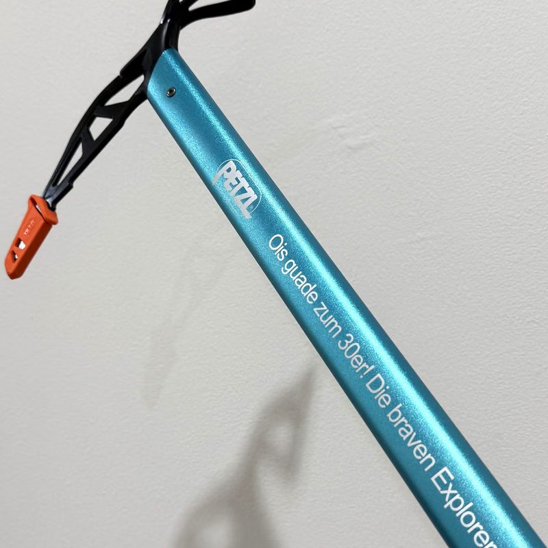 Ein hellblauer Eispickel mit eingraviertem Schriftzug, an einer Wand lehnend