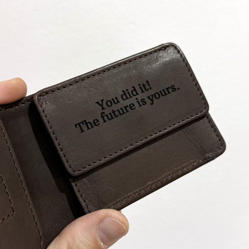 Eine dunkelbraune Geldbörse aus Leder mit der eingravierten Zeile „You did it! The future is yours.“