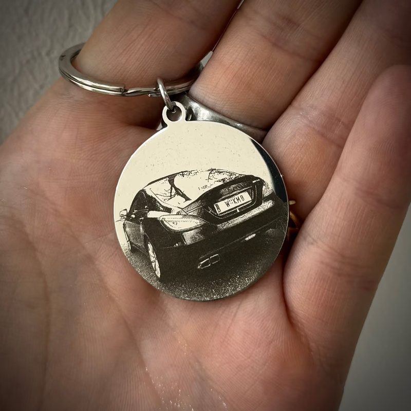 Runder Schlüsselanhänger aus Metall mit der Fotogravur eines Autos, in der Hand gehalten