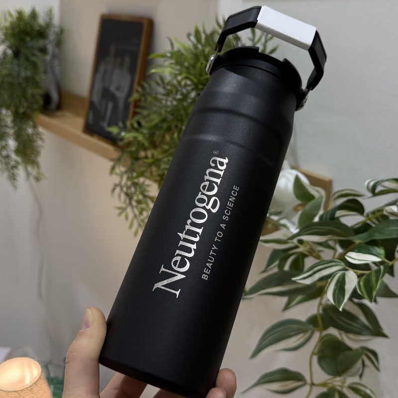 Eine schwarze Trinkflasche mit graviertem Firmenlogo, in der Hand gehalten